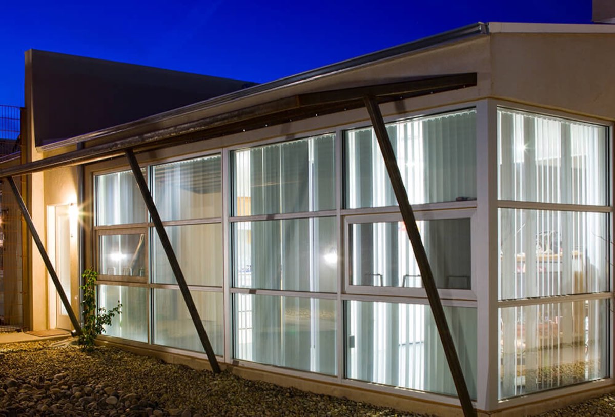 Glass-walled community building at Lolomas glowing from within at dusk